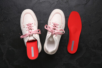 Sneakers and red orthopedic insoles on black grunge background