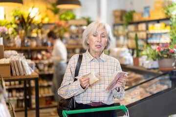 Elderly woman buyer chooses fresh cheese and bacon meat in eco grocery supermarket