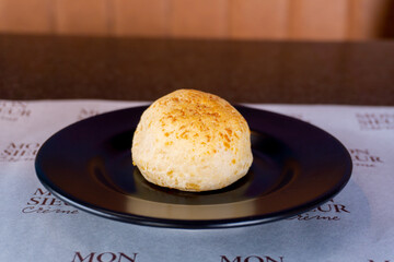 A delicious pao de queijo rests on a black plate, ready to be enjoyed.