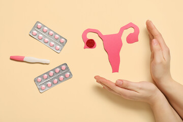 Female hands with paper uterus, pregnancy test and pills on beige background