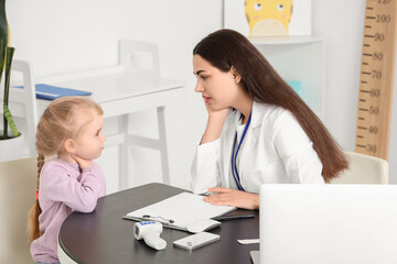 Fototapeta premium Female pediatrician and little girl with sore throat at table in clinic