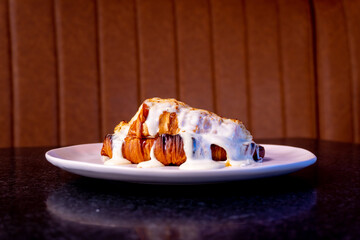 A golden croissant, generously coated with creamy cheese sauce, on a white plate.