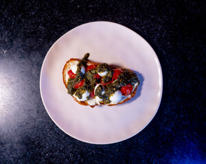 A delicious bruschetta, a perfect Italian appetizer, topped with pesto, tomatoes, and mozzarella.