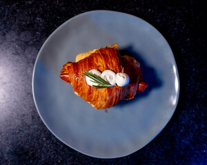 A golden, flaky croissant with cream and rosemary on a blue plate.