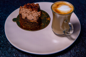 Chocolate cake slice and latte sit invitingly on a plate, ready to be enjoyed.