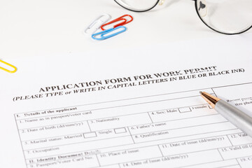 An application form for a work permit rests on a desk alongside a pen, symbolizing employment...