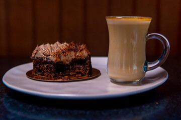 A delicious slice of cake paired with a frothy latte on a white plate, perfect for a relaxing morning.