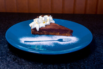 A delectable slice of chocolate tart, beautifully presented on a blue plate with a fork design.