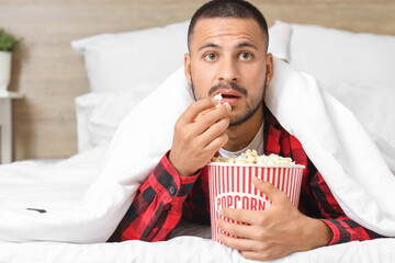 Young man with popcorn watching movie in bed