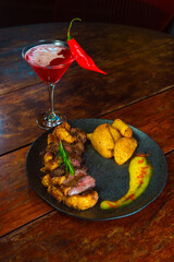 A beautifully presented steak dinner is served with a vibrant cocktail and a chili pepper.