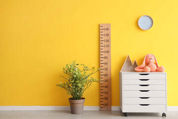 Toys on commode with wooden stadiometer near yellow wall in children's room