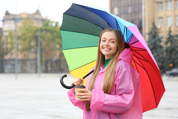 Beautiful young happy woman in raincoat with umbrella on rainy day outdoors