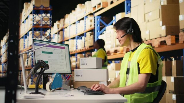 Call center male worker answer help line calls in a logistics warehouse, updating clients on orders and resolving cargo mix ups. Managing shipping software and airway bills. Camera A.