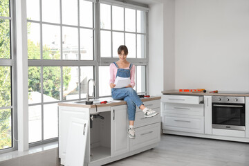 Young woman with furniture assembly plan sitting on counter in kitchen
