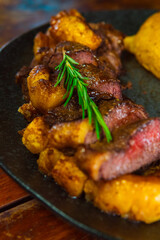 A delicious steak with roasted potatoes and rosemary garnish on a black plate.