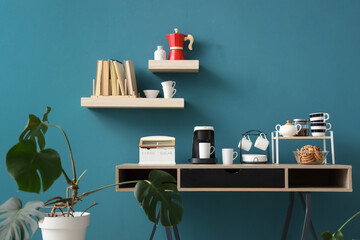 Coffee machine with cups and cookies on table near blue wall in room