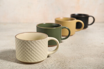 Different ceramic mugs on light grunge background