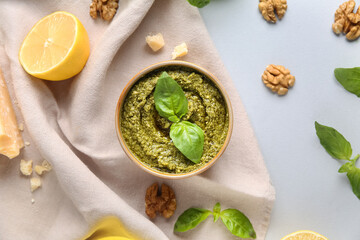 Bowl of delicious pesto sauce with walnuts, cheese and basil leaves on white background