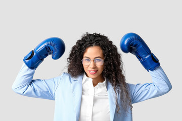 Young African-American businesswoman with boxing gloves on light background. Knockout concept