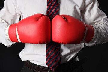 Young businessman with boxing gloves on black background, closeup. Knockout concept