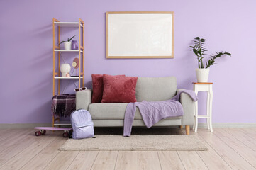 Stylish sofa, rack with decor, houseplant and blank poster on lilac wall