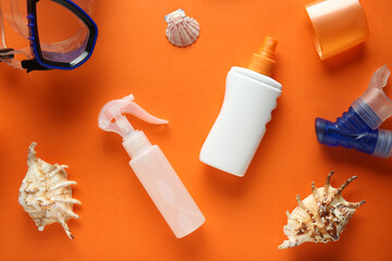 Composition with seashells and bottles of sunscreen cream on orange background