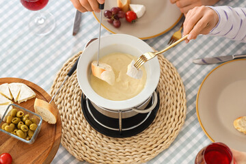 Young couple with glasses of wine dipping croutons into cheese fondue at home, top view