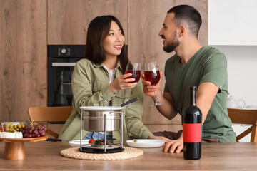 Young happy couple with glasses of wine, snacks and cheese fondue at home