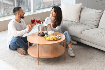 Young happy couple with glasses of wine dipping marshmallows into chocolate fondue at home
