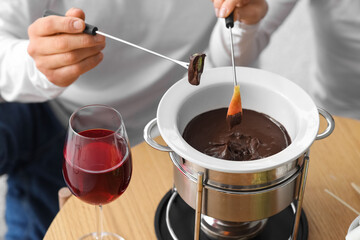 Young couple with glasses of wine dipping fresh fruits into chocolate fondue at home, closeup