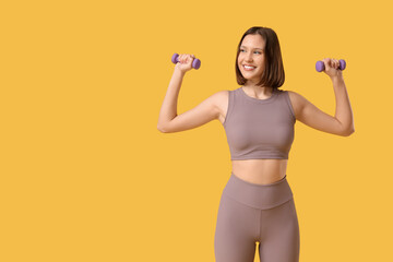 Sporty young woman with dumbbells on yellow background