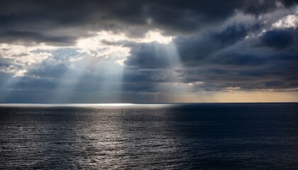 Obraz premium rays of sunlight break through dark clouds over a tranquil ocean at midday