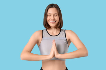 Sporty young woman doing yoga on blue background