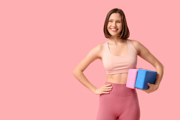 Sporty young woman with yoga blocks on pink background