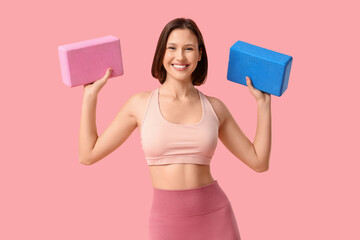 Sporty young woman with yoga blocks on pink background