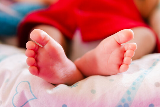 Peque&ntilde;a beb&eacute; reci&eacute;n nacida con un vestidito rojo muestra sus diminutos pies descalzos sobre una manta blanca y rosa. Una imagen tierna que simboliza nueva vida y pureza