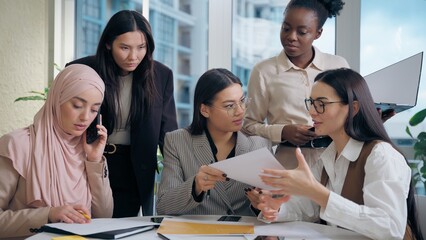 Multiethnic women females team girls African American Japanese Caucasian Arabian businesswomen discussing project plan paperwork document working meeting talk Muslim hijab woman mobile phone in office
