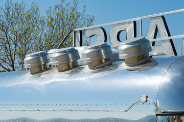 Shiny metallic vents on a curved, reflective surface with a blue sky and green trees visible in the...