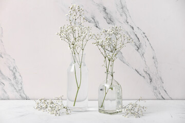 Glass vases with beautiful gypsophila flowers on white table near marble wall
