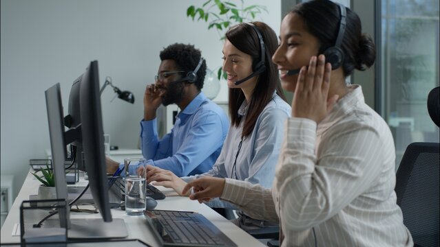 Callcenter helping agents business helpline call center multiethnic people happy Indian Caucasian women in headset African man consulting customer client work computer phone writing notes pen office
