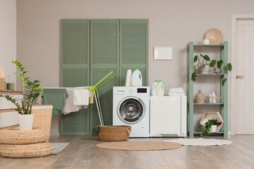 Interior of stylish laundry room with modern washing machine, dryer and bathing accessories