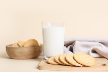 Wooden board with sweet cookies and glass of fresh milk on beige background