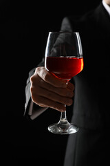 Businessman holding glass of wine on black background