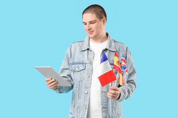 Young man with tablet computer and flags of different countries on color background