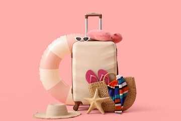 Suitcase with starfish, inflatable ring and beach accessories on pink background