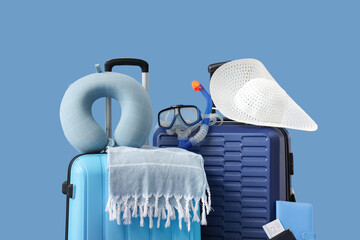 Suitcases, travel pillow and beach accessories on blue background, closeup