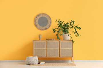 Houseplant and statuette on chest of drawers near yellow wall in room