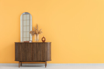Mirror and pampas grass on chest of drawers near yellow wall in interior of room