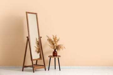 Big floor mirror and vase with pampas grass on table near beige wall in room