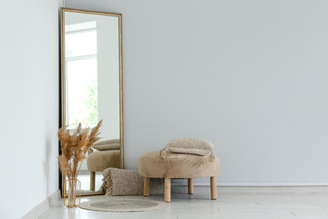 Floor mirror, vase with pampas grass and pouf near white wall in room
